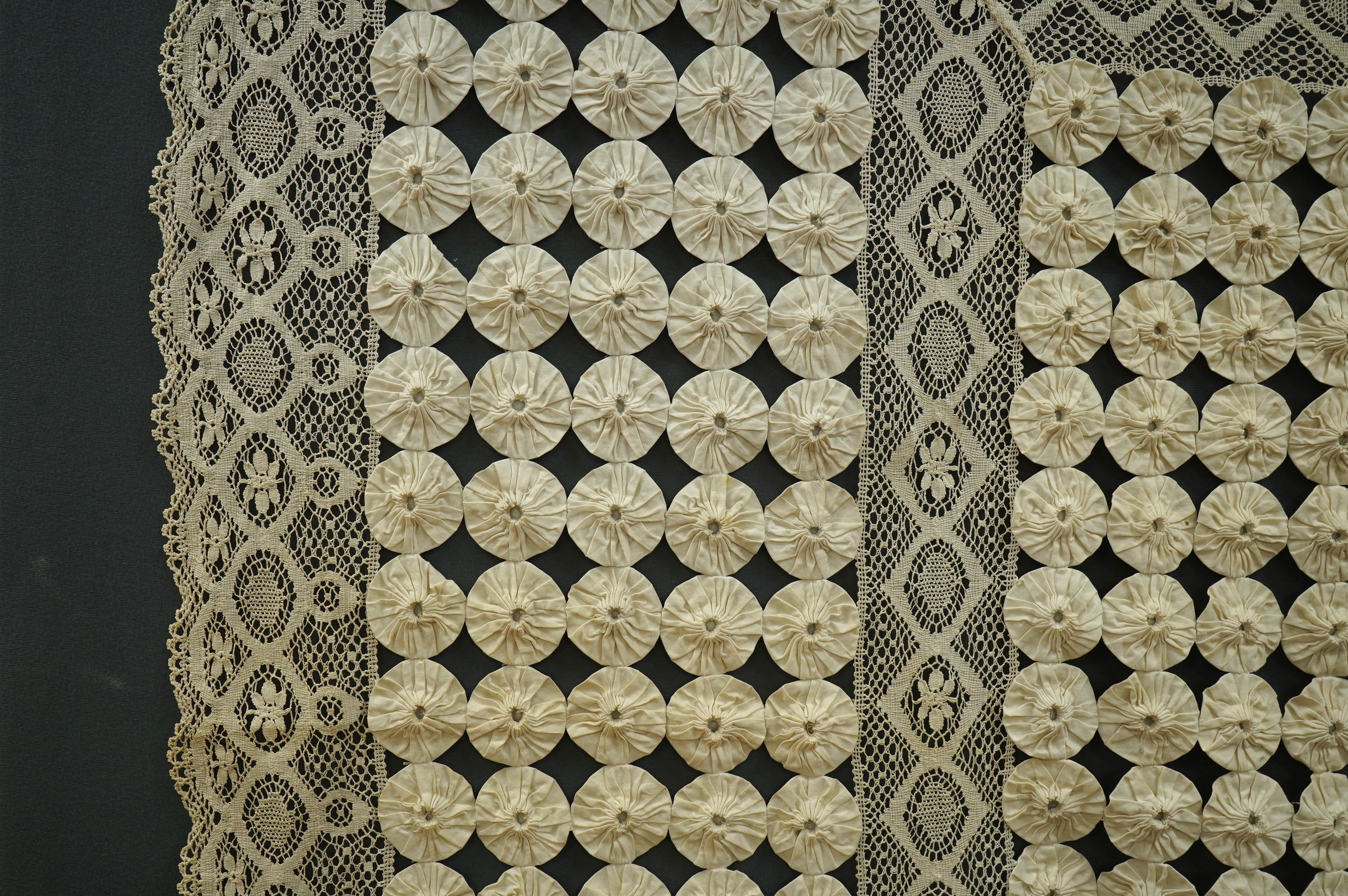 A late 19th early 20th century ‘YoYo’ puffy cream silk and cream bobbin lace quilt/bedcover, made with circles of silk, drawn together as a decorative gathered to top, then stitched together in panels and between wide bo